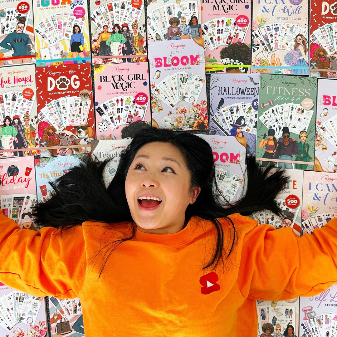 Woman surrounded by sticker books, including Black Girl Magic and Bloom