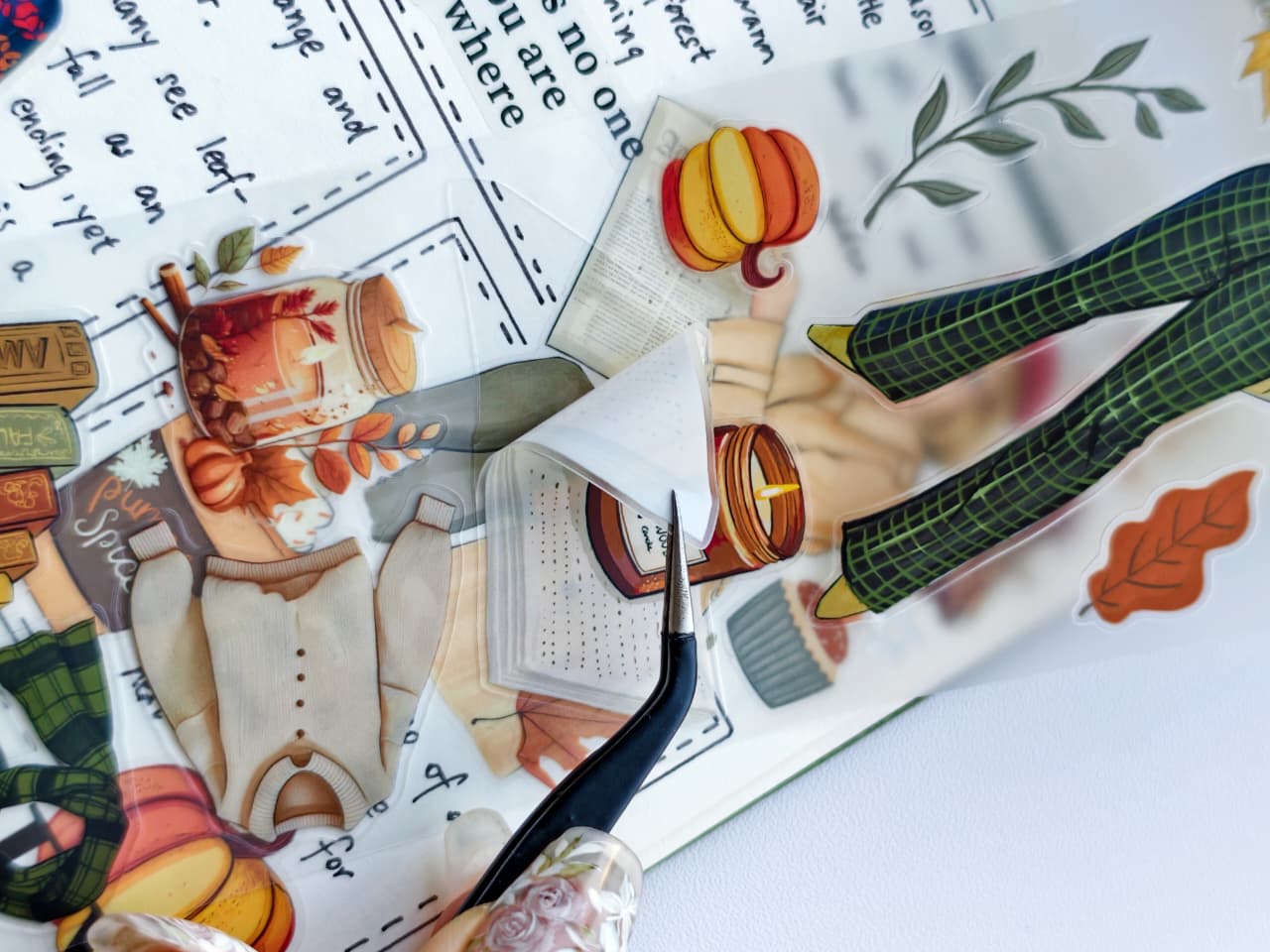 Macro view of Amber Allure pre-cut PET tape with tweezers lifting a transparent autumn-themed sticker, highlighting the easy peel design for planners, journals, and scrapbooks.