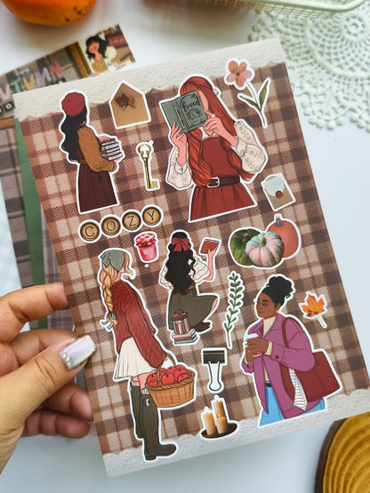 Close-up of the Autumn Moments vinyl sticker sheet showcasing cozy autumn-themed character stickers, pumpkins, coffee, books, candles, and seasonal decorative elements.