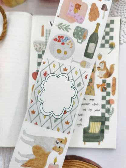 Close-up of Cozy Cottage Washi Tape showcasing watercolor illustrations of breakfast, hot drinks, wine bottle, autumn leaves, decorative journaling label, puppy, candle, and cozy seasonal motifs.
