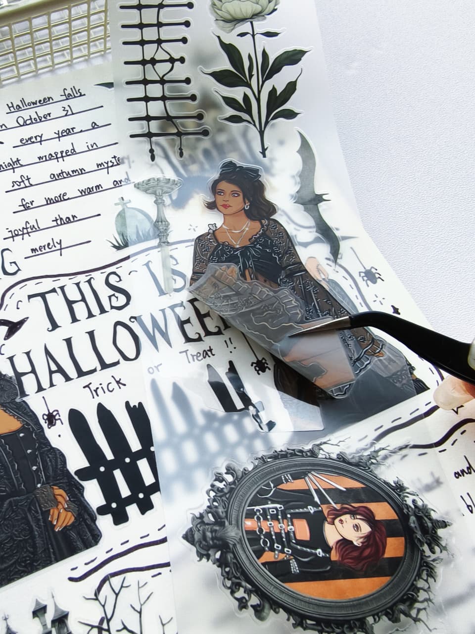 Macro view of Creepy Hollow pre-cut PET tape with tweezers peeling a transparent gothic fashion sticker surrounded by haunted Halloween illustrations, bats, spooky portraits, and vintage accents.