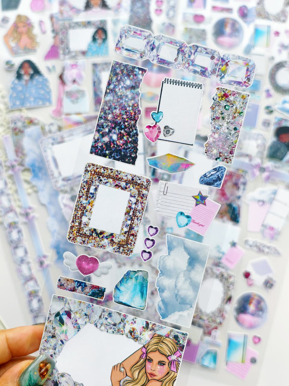Close-up of transparent crystal-themed stickers featuring glitter textures, gem frames, sparkly hearts, clouds, holographic diamonds, and decorative journaling pieces.