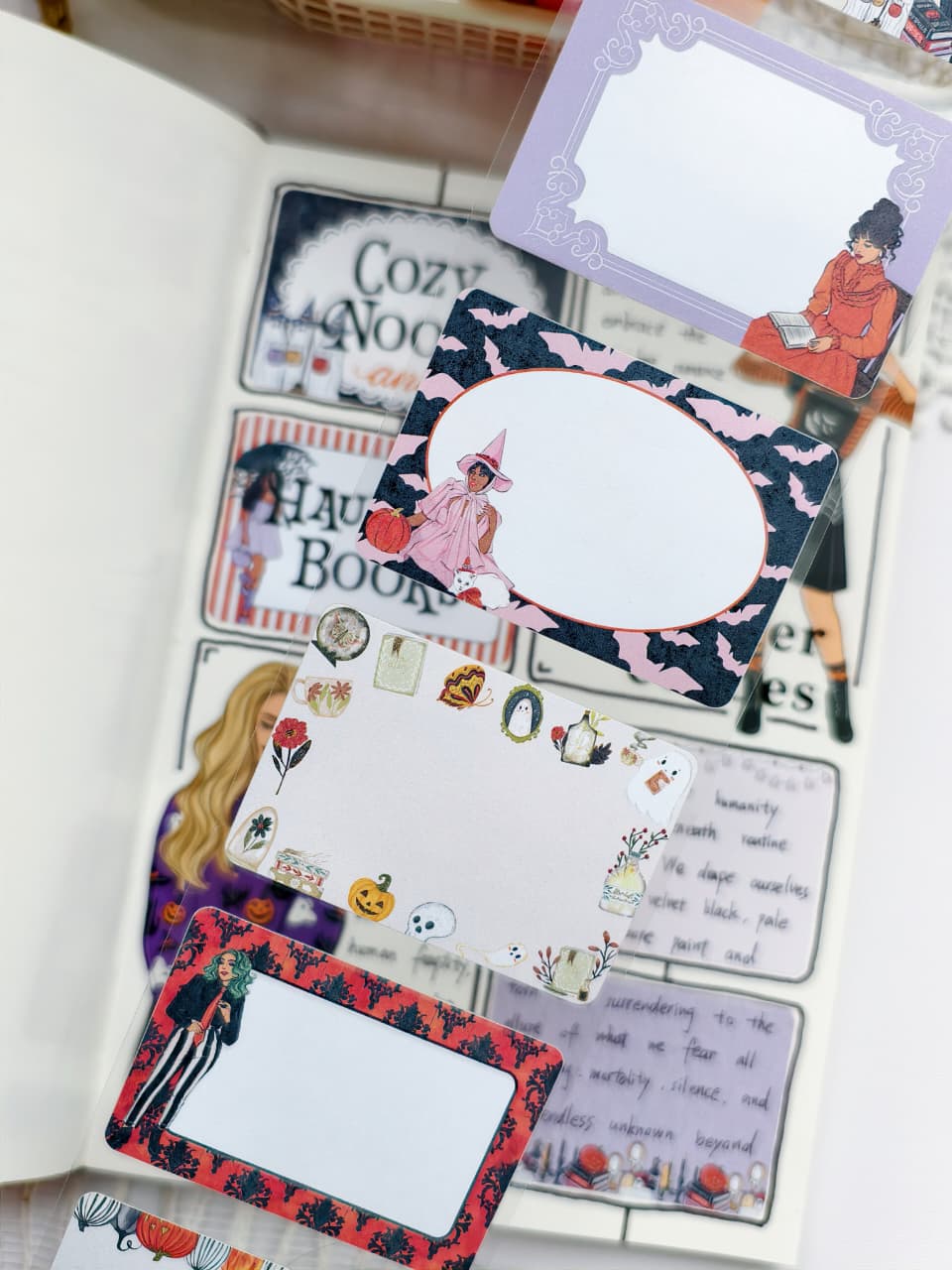 Close-up of Halloween-themed sticky notes showcasing ornate frames, spooky icons, and illustrated characters, displayed over a decorated journal spread with pumpkins and gothic accents.