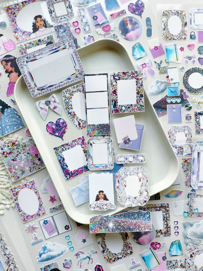Crystal Haze ephemera stickers displayed on a tray with holographic frames, glitter labels, gem-inspired shapes, pastel clouds, and feminine scrapbook accents.
