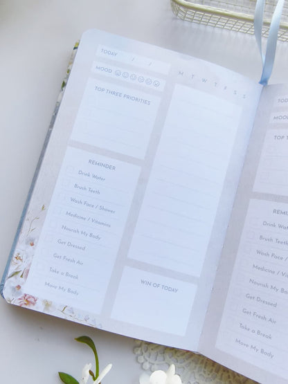 An open Gentle Focus journal displaying a clean daily planning page with sections for mood tracking, top priorities, reminders, a daily schedule, and a "Win of Today" reflection. The soft pastel layout and minimalist design create a calm and organized planning experience.