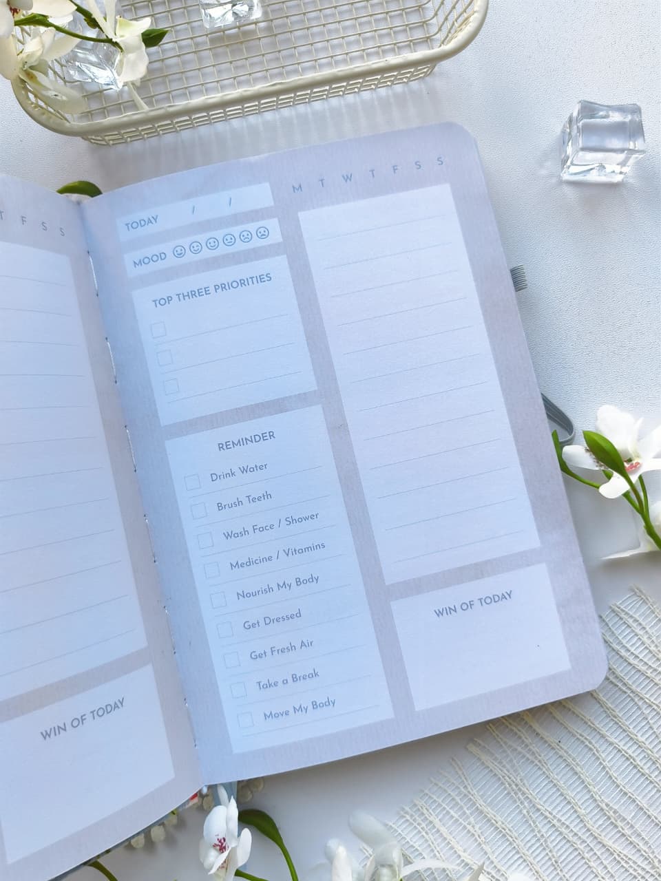 An open Gentle Focus journal featuring a beautifully organized daily planning page with sections for mood tracking, top three priorities, reminders, a timed schedule, and a "Win of Today" reflection. The soft pastel colors, floral accents, and minimalist layout create a peaceful and inspiring space for daily planning.