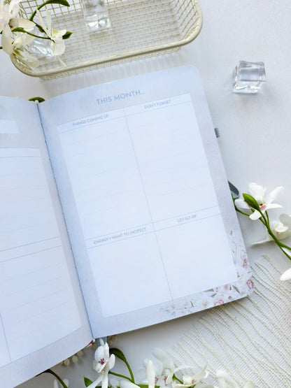 An open Gentle Focus journal displaying a monthly planning page with dedicated sections for monthly goals, due dates, projects and habits, and notes. Soft floral accents along the bottom edge and a clean pastel layout create a calm, elegant space for organizing the month ahead.