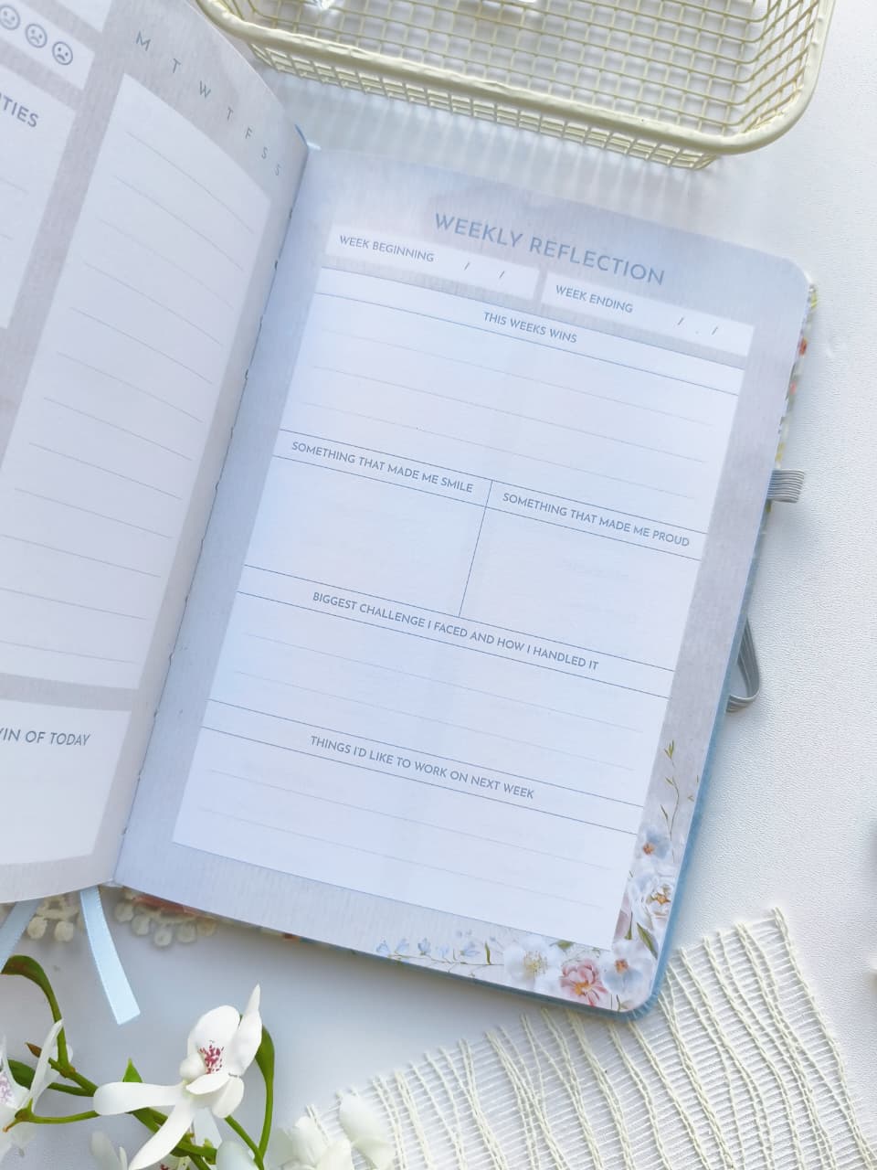 An open Gentle Focus journal displaying a Weekly Reflection page with prompts to review the week, celebrate accomplishments, reflect on lessons learned, and set goals for the week ahead. The soft pastel design, floral border, and clean layout provide a calming space for mindful reflection and planning.