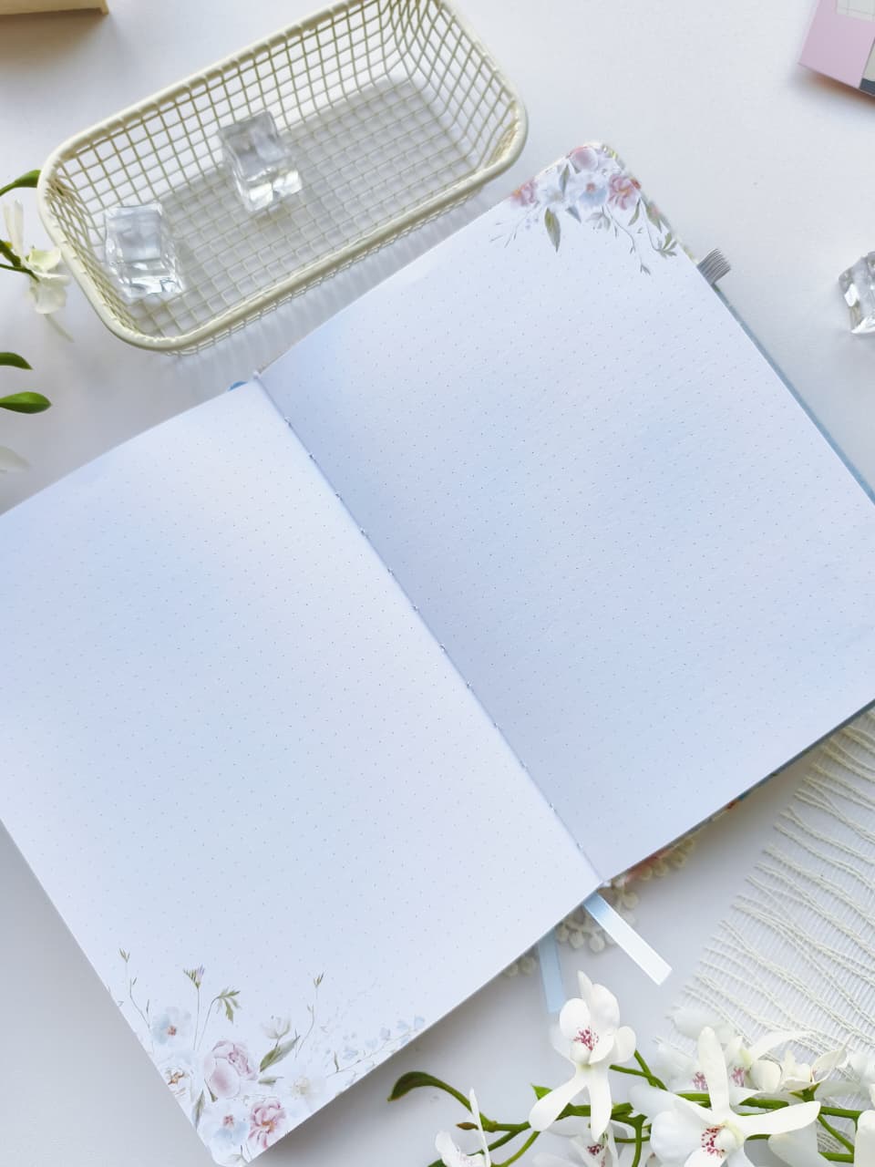 An open Gentle Focus journal displaying two dotted note pages with delicate floral accents in the corners. The clean, minimalist layout provides plenty of space for journaling, note-taking, sketching, or creative planning, all styled on a bright white surface with elegant floral décor.