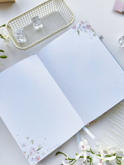 An open Gentle Focus journal displaying two dotted note pages with delicate floral accents in the corners. The clean, minimalist layout provides plenty of space for journaling, note-taking, sketching, or creative planning, all styled on a bright white surface with elegant floral décor.