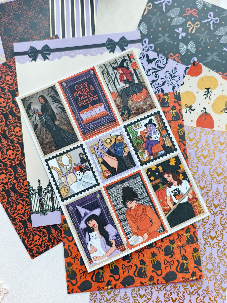 A flat lay of Halloween-themed patterned papers and a central printed card featuring vintage witch illustrations. The designs include orange cat silhouettes, black bats, purple witch portraits, pumpkins, stripes, bows, and ornate motifs on a white surface.