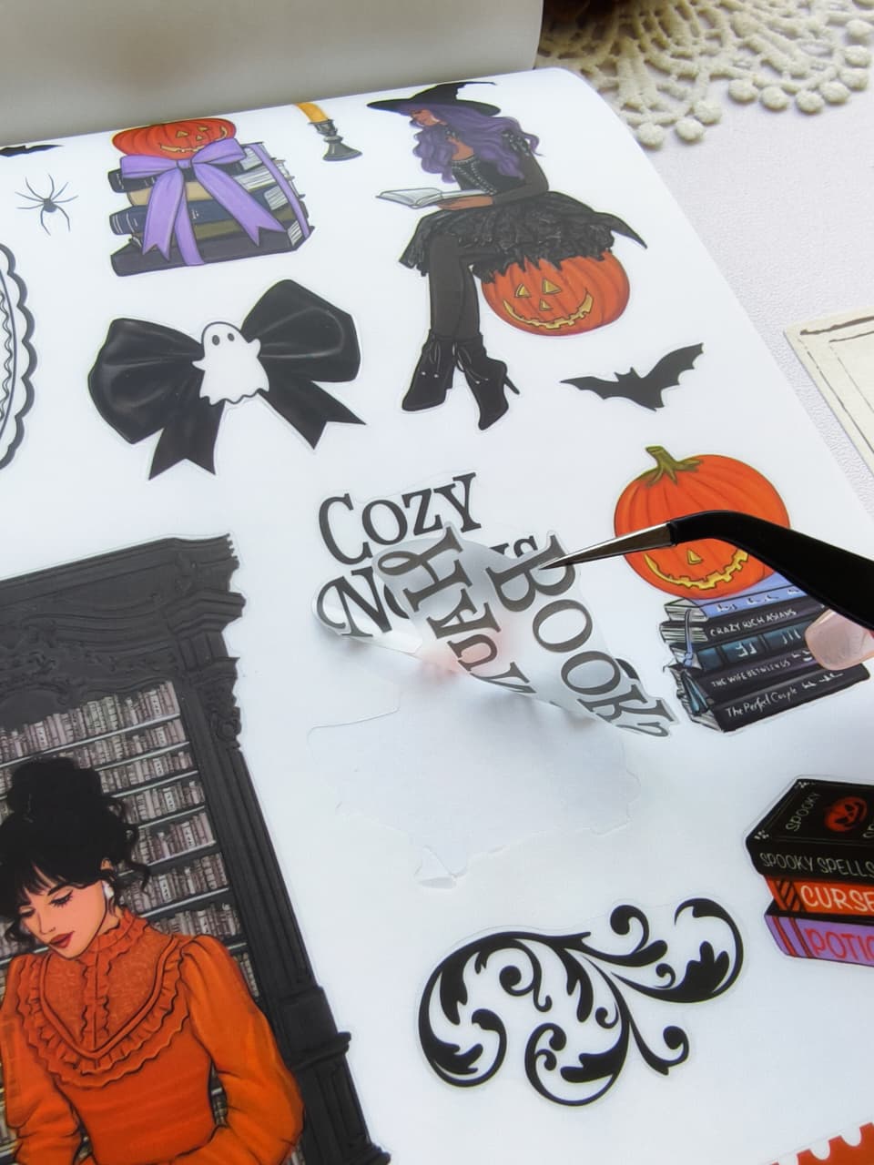 Halloween-themed sticker book page featuring witches, pumpkins, books, black bows, bats, cozy reading illustrations, spooky typography, and decorative Halloween embellishments.