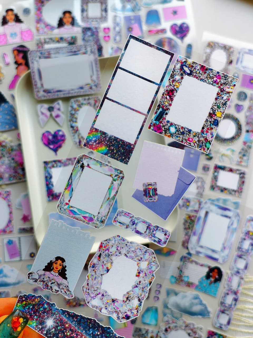 Close-up of transparent sticker sheet featuring sparkling crystal frames, glitter borders, holographic gems, pastel journaling cards, and dreamy decorative elements.