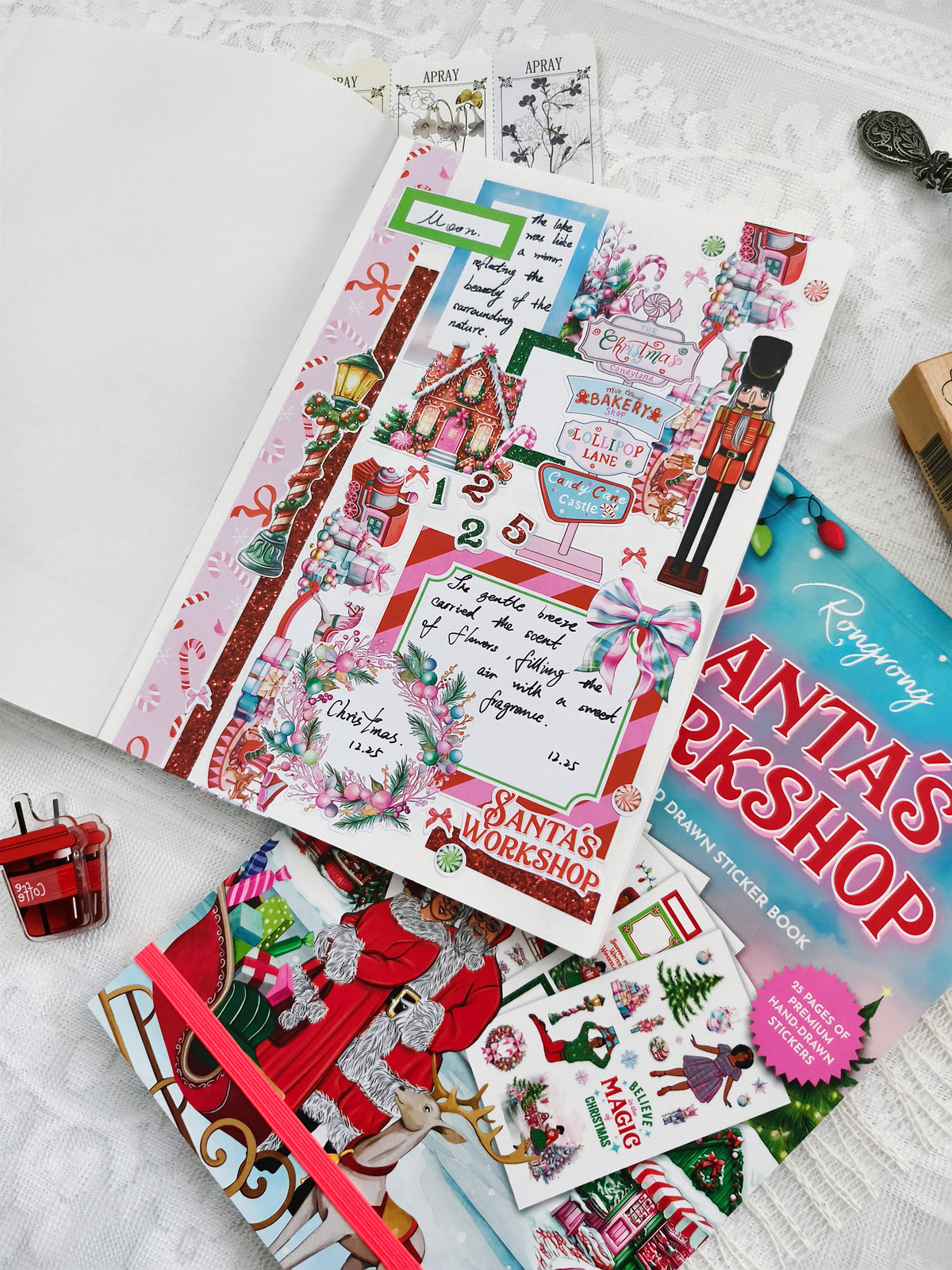 Collection of Christmas-themed stationery items including stickers and a book titled 'Santa's Workshop' on a white surface.