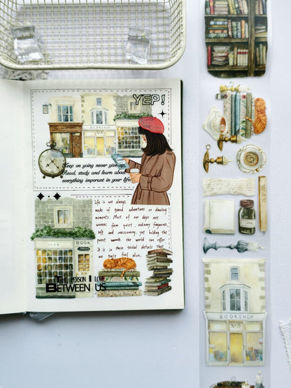 Open journal decorated with Magic Library Pre-cut PET Tape featuring a charming bookshop storefront, vintage clock, book lover illustration, stacked books, and cozy literary elements in a warm cottagecore aesthetic.