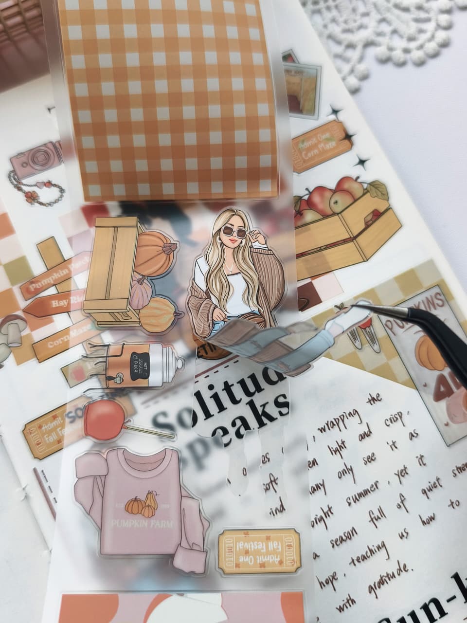 Close-up of tweezers lifting a Fall Festival PET Tape sticker from its backing, highlighting the transparent PET material and easy-peel design featuring a cozy autumn fashion illustration.