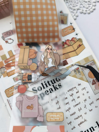 Close-up of tweezers lifting a Fall Festival PET Tape sticker from its backing, highlighting the transparent PET material and easy-peel design featuring a cozy autumn fashion illustration.