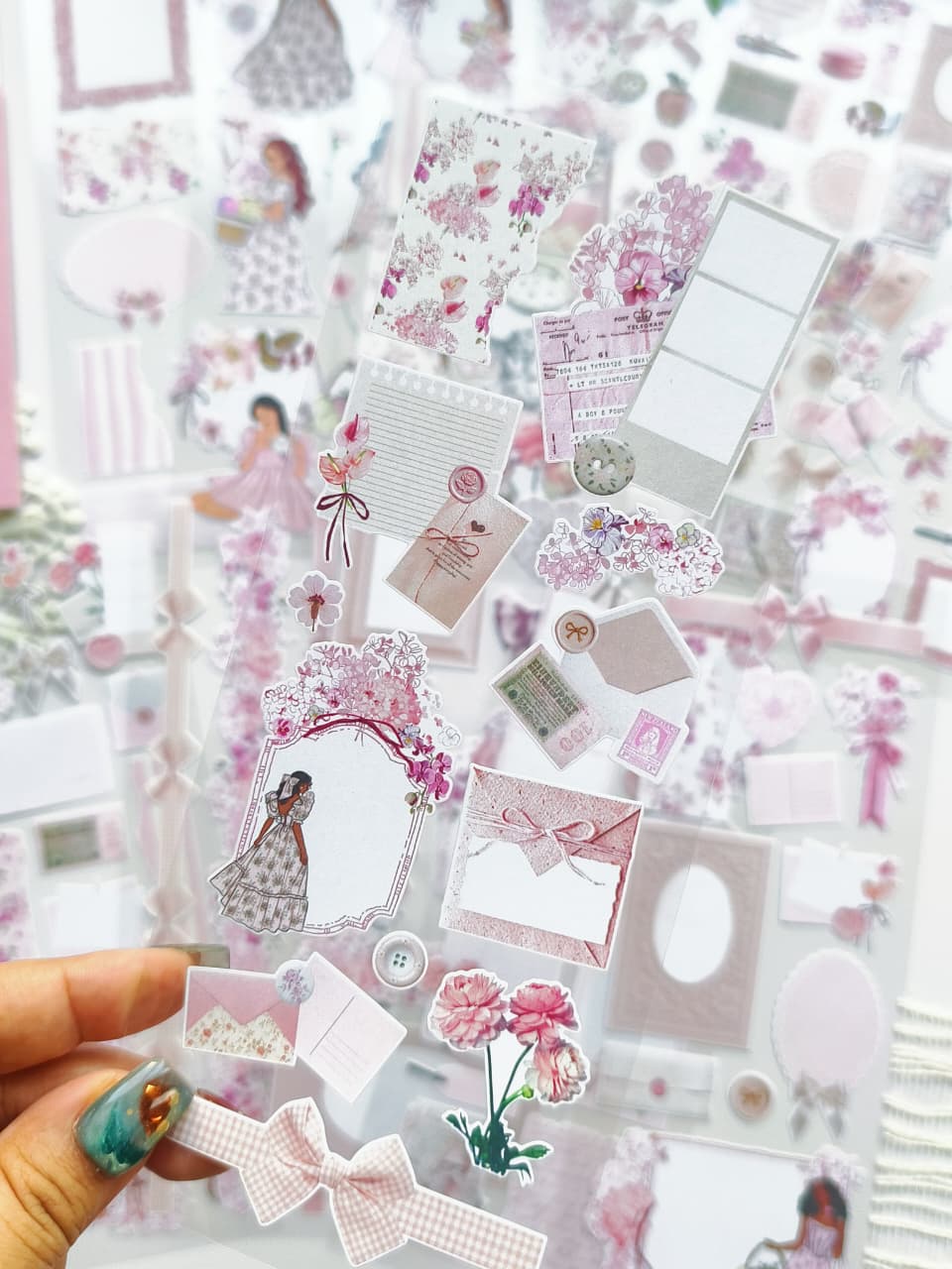 Close-up of transparent pink ephemera stickers featuring floral labels, bows, envelopes, vintage-inspired paper pieces, and delicate decorative accents.