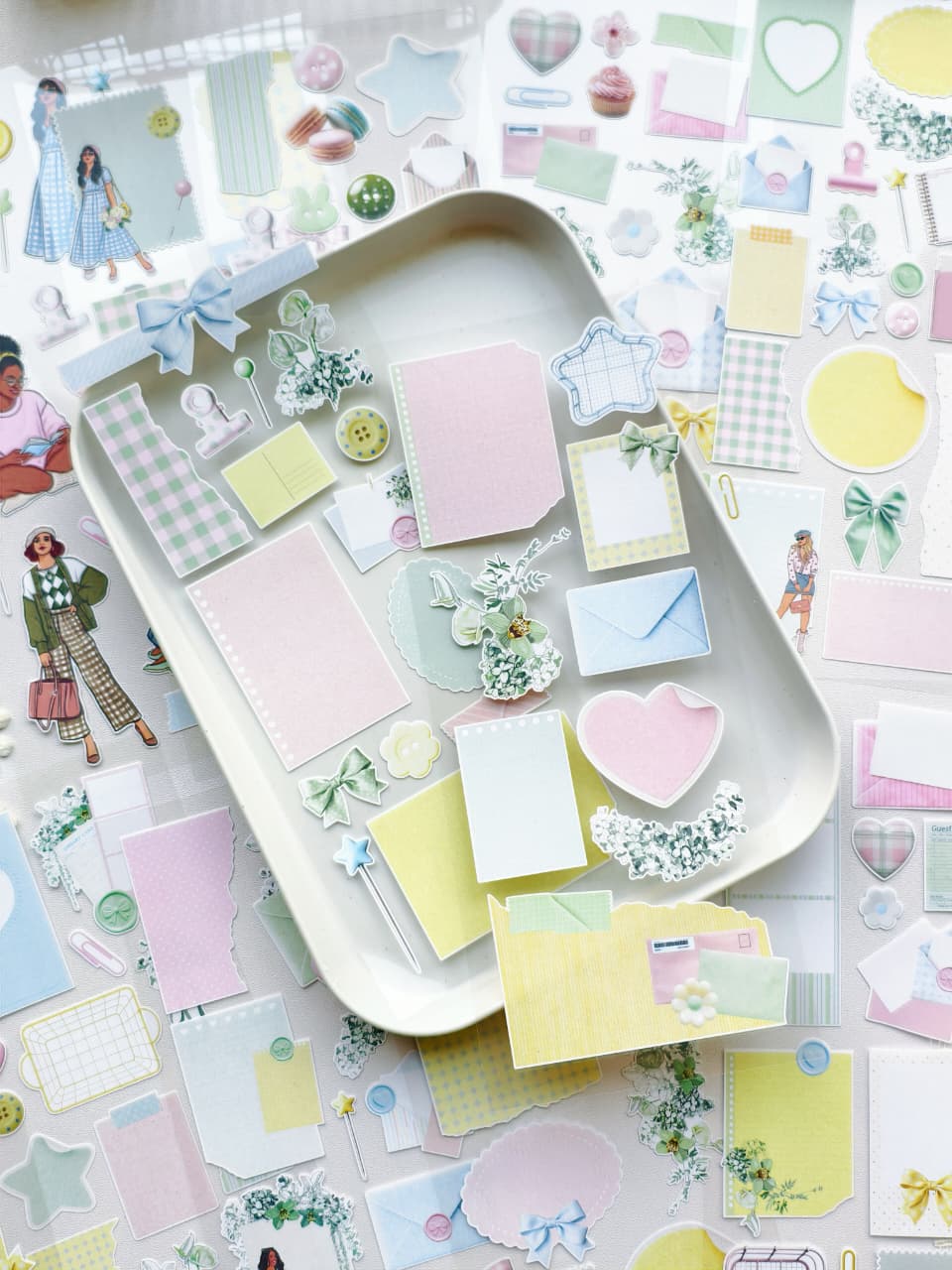 Decorative pastel ephemera stickers displayed on a tray featuring memo papers, envelopes, florals, bows, hearts, and scrapbook-style journaling pieces.