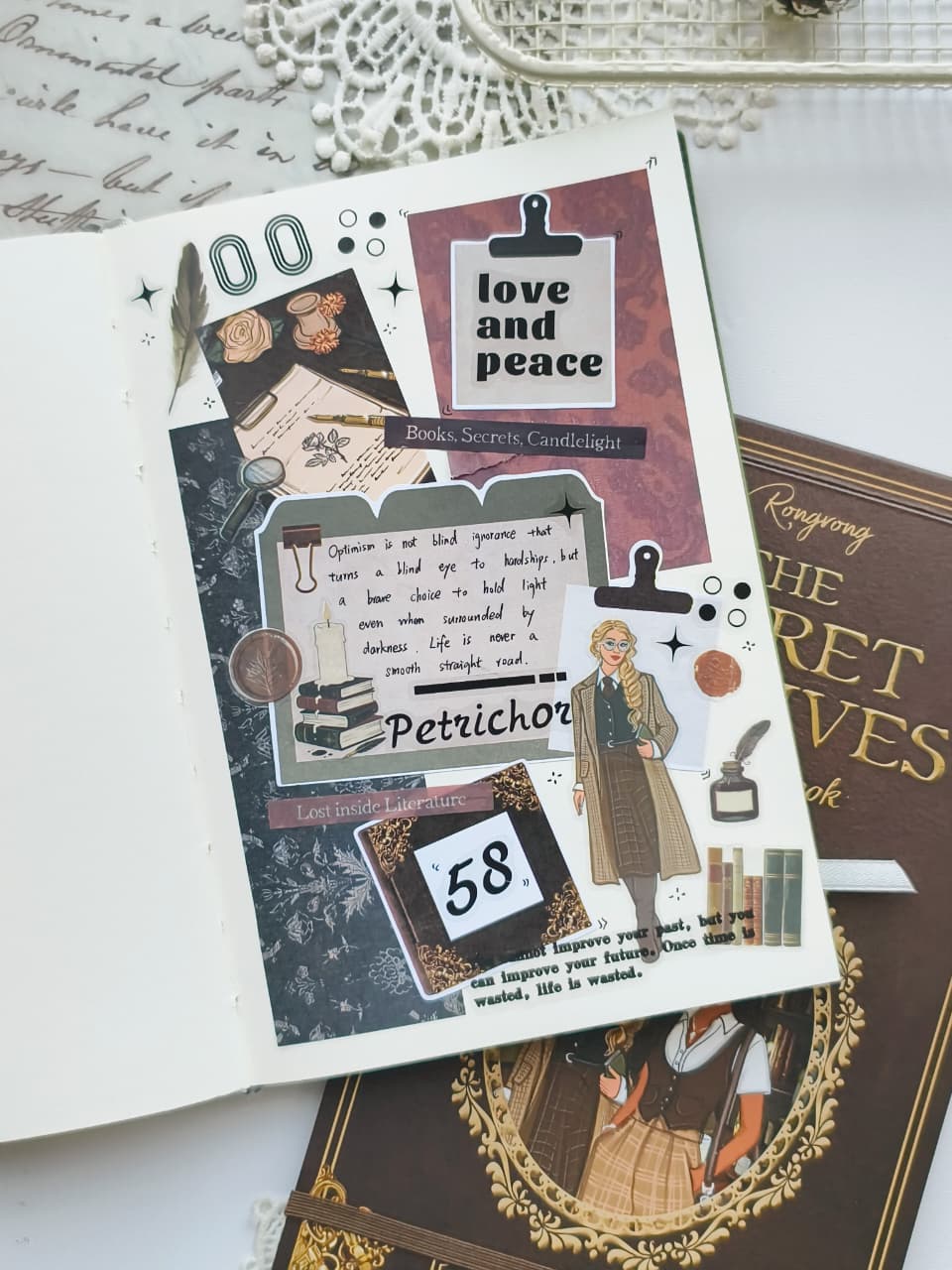 An open book or journal spread showing a decorative collage page with vintage-style paper clips, handwritten notes, a small illustrated figure, the words &