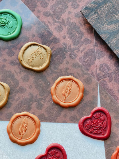 A styled flat-lay of wax seals in multiple colors, including green, gold, orange, and red, arranged on patterned brown paper and a white surface.