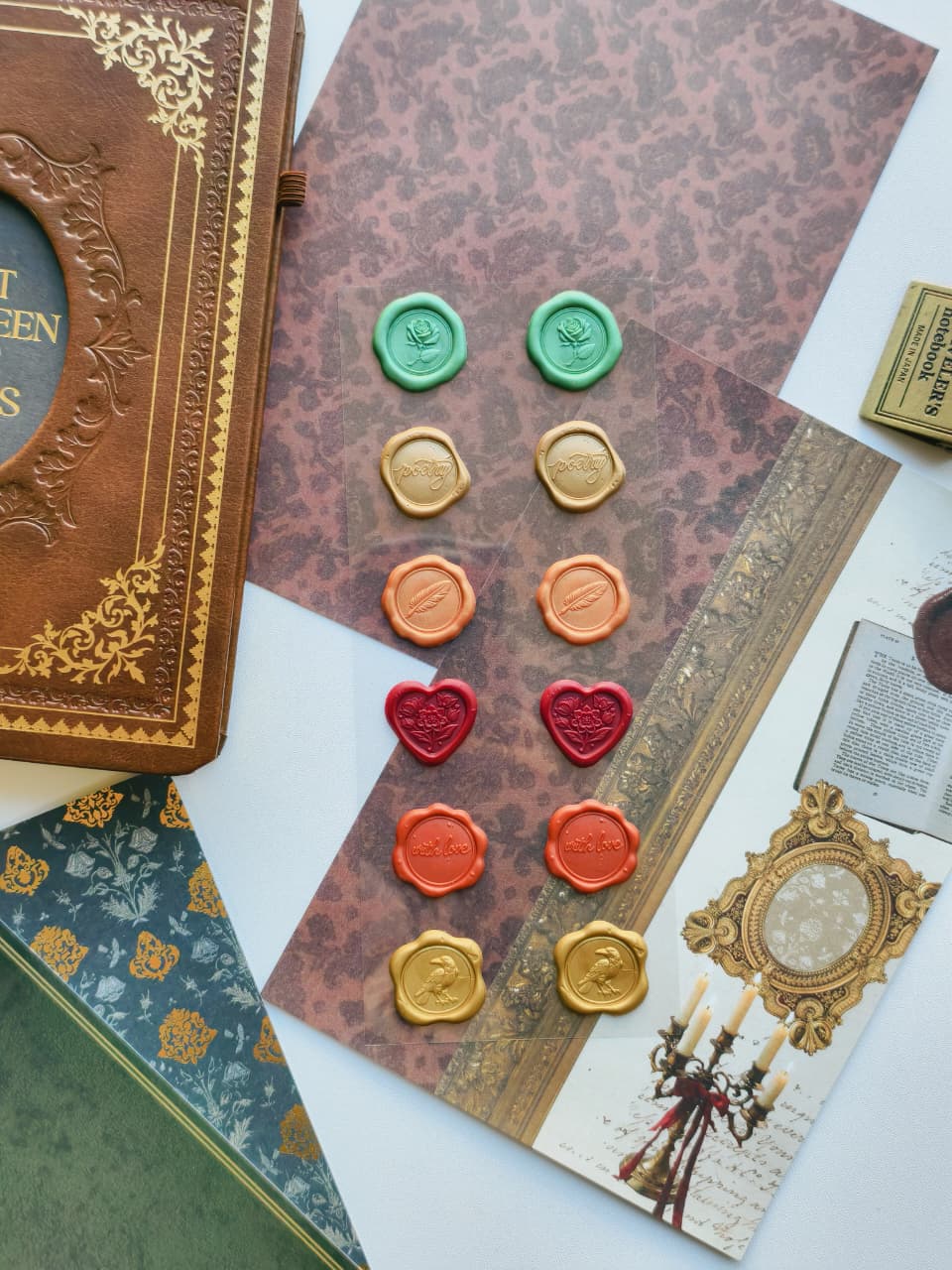 A styled flat-lay of vintage wax seals arranged on patterned paper sheets next to antique-style books and decorative prints.