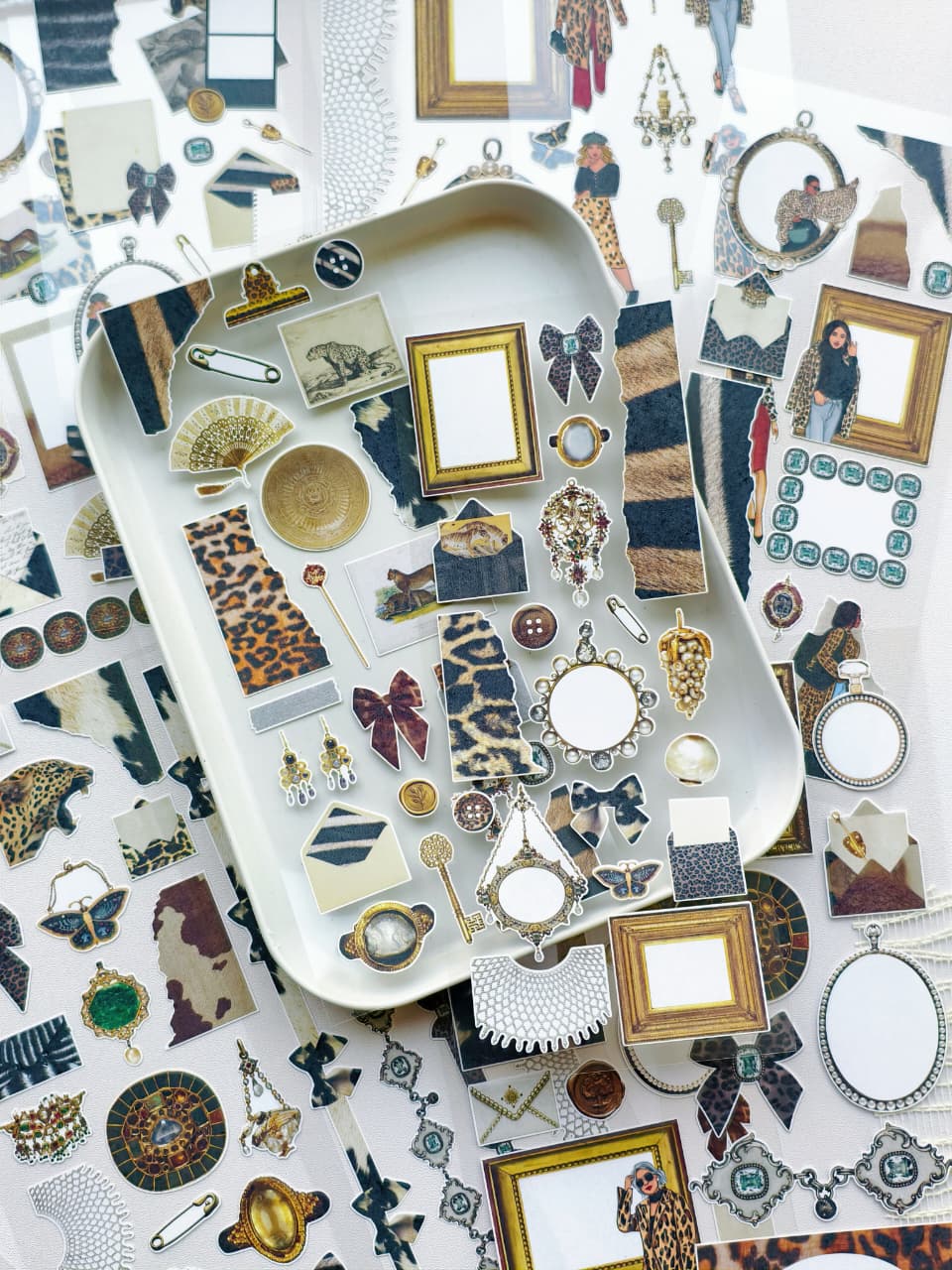 Decorative planner stickers displayed on a tray featuring leopard print textures, vintage frames, jewelry-inspired accents, bows, and collage elements.