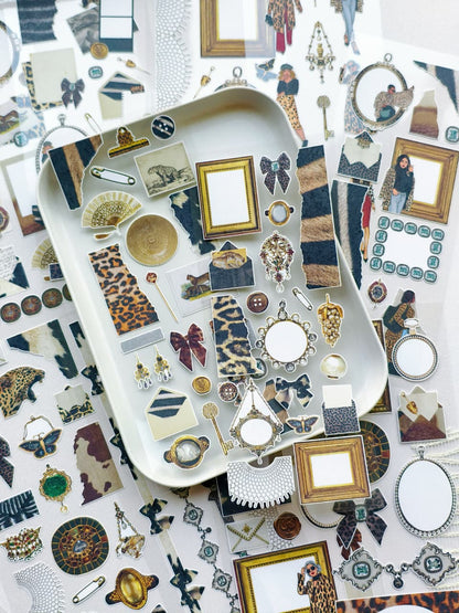 Decorative planner stickers displayed on a tray featuring leopard print textures, vintage frames, jewelry-inspired accents, bows, and collage elements.