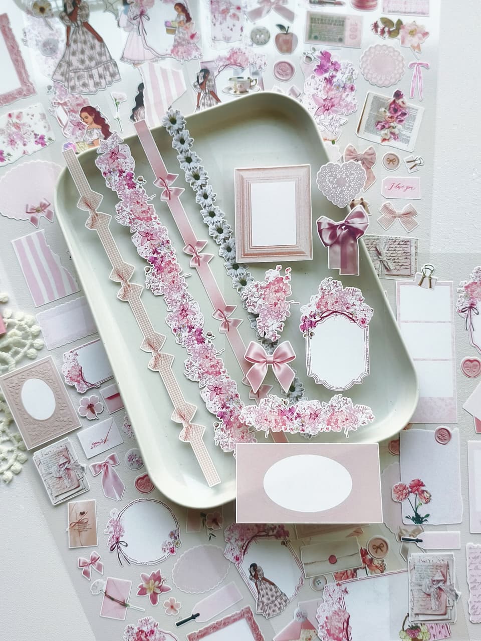 Pink romantic ephemera stickers displayed on a tray with floral garlands, bows, ornate frames, memo papers, and vintage scrapbook-inspired embellishments.