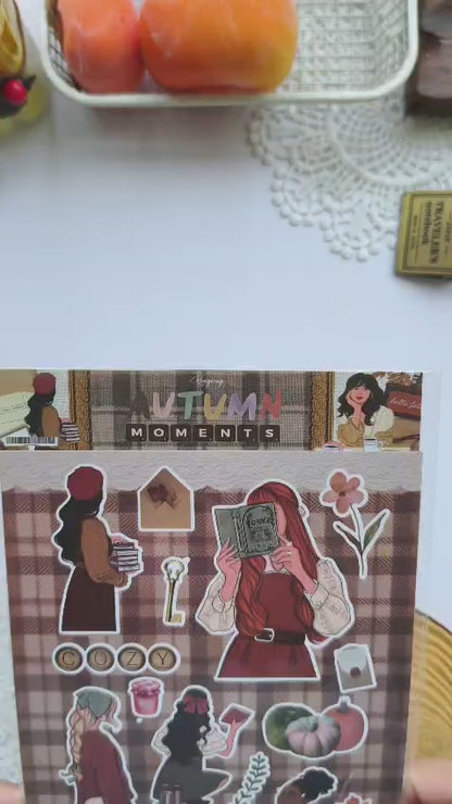 Showcase video featuring the Autumn Moments vinyl sticker sheet with premium kiss-cut stickers, cozy autumn characters, books, coffee, candles, pumpkins, scarves, woodland accents, and fall-inspired illustrations for planners, journals, scrapbooks, and paper crafting.
